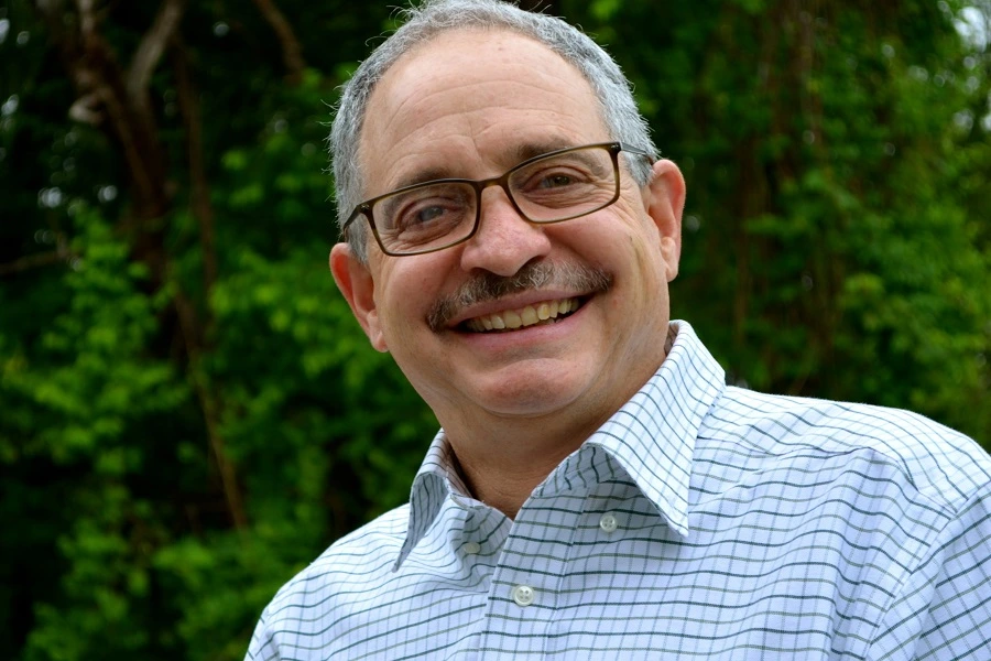 mature man in check shirt smiling with trees in background